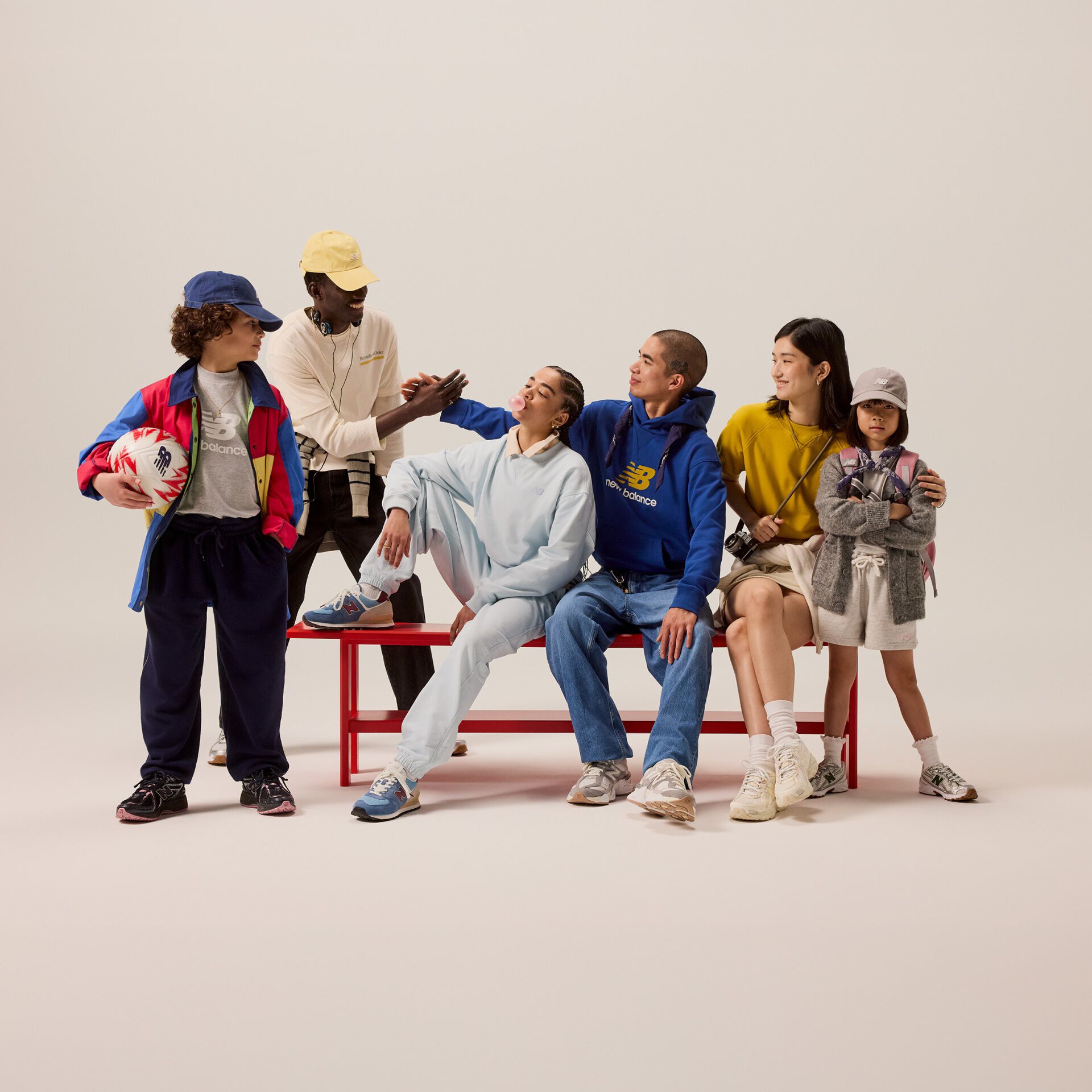 Group of students sitting on a red bench in front of a beige background.